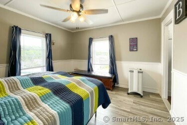 25 Myrtle Ave, Ansonia, CT 06401 - bedroom with radiator heating unit, light wood finished floors, crown molding, a wainscoted wall, and ceiling fan