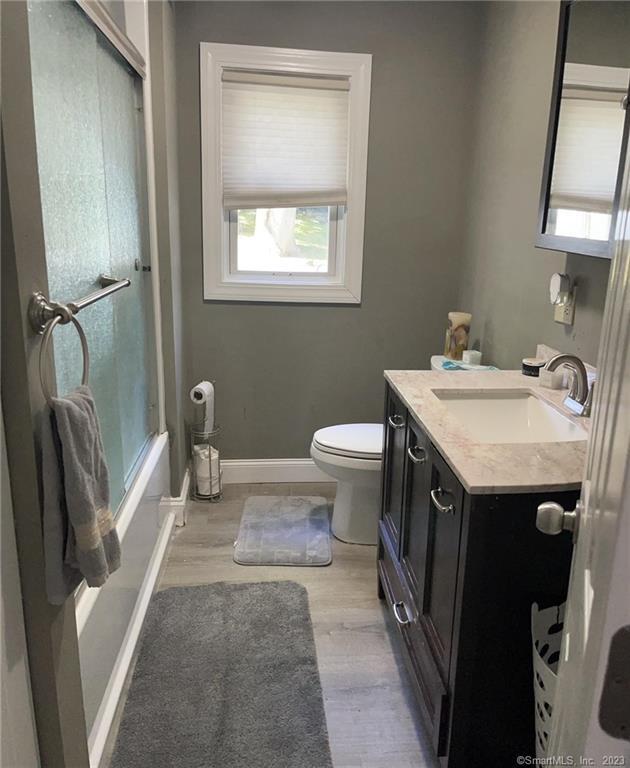 665 W Main St, West Haven, CT 06516 - full bath featuring vanity, toilet, wood finished floors, baseboards, and combined bath / shower with glass door