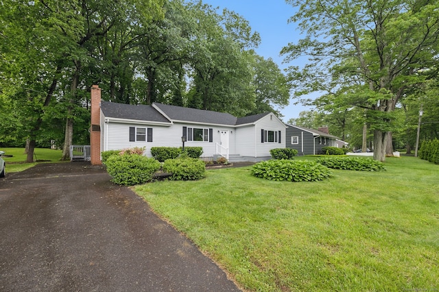 view of front of home featuring a chimney, a front yard, driveway, view of wooded area, and roof with shingles