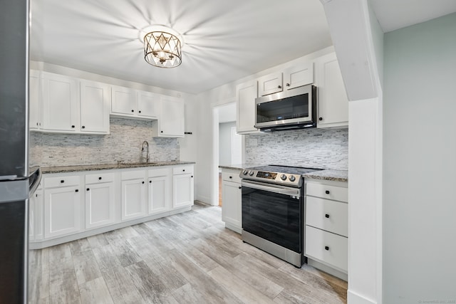 kitchen featuring appliances with stainless steel finishes, a sink, light stone countertops, and tasteful backsplash