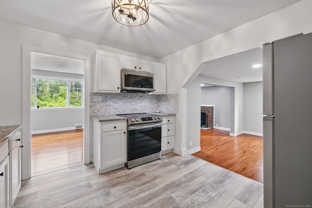 kitchen with stainless steel appliances, light wood-style flooring, decorative backsplash, white cabinetry, and baseboards
