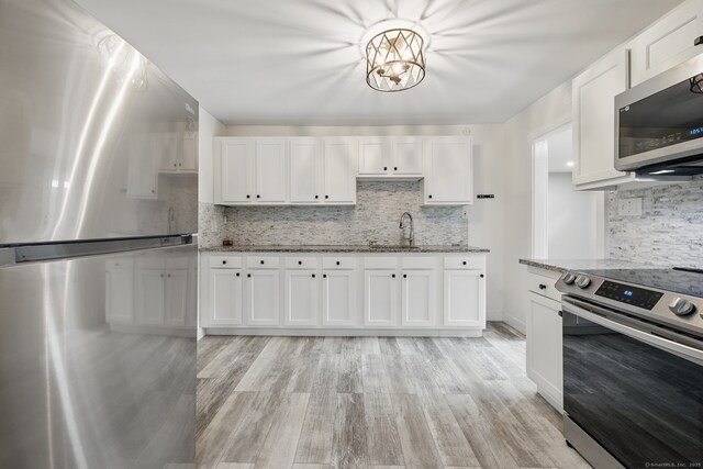 kitchen featuring stainless steel appliances, a sink, decorative backsplash, and white cabinetry
