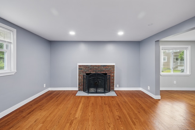 unfurnished living room with wood finished floors, baseboards, a brick fireplace, and recessed lighting