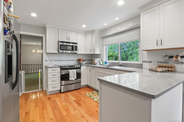 1704 Hill St, Suffield, CT 06078 - kitchen with appliances with stainless steel finishes, a peninsula, backsplash, light wood-style floors, and white cabinetry