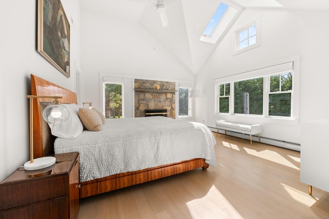 27 Quarry Rd, Stonington, CT 06355 - bedroom with a skylight, high vaulted ceiling, wood finished floors, a baseboard radiator, and a stone fireplace