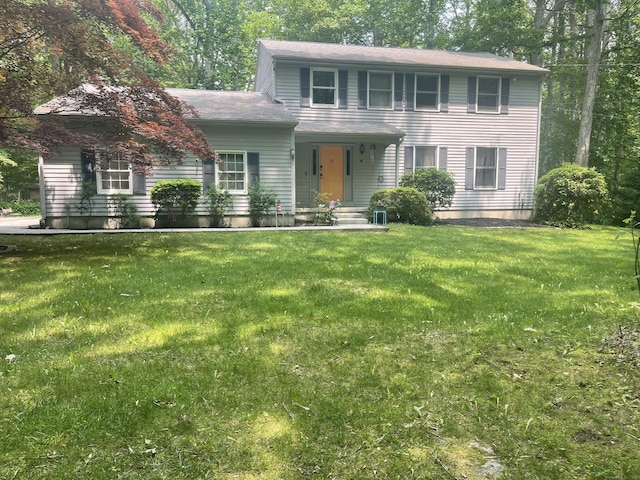 colonial house featuring a front yard and roof with shingles
