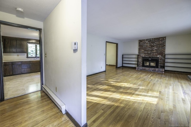 58 Wildwood Ln, Durham, CT 06422 - unfurnished living room featuring a baseboard heating unit, light wood-type flooring, a brick fireplace, and baseboards