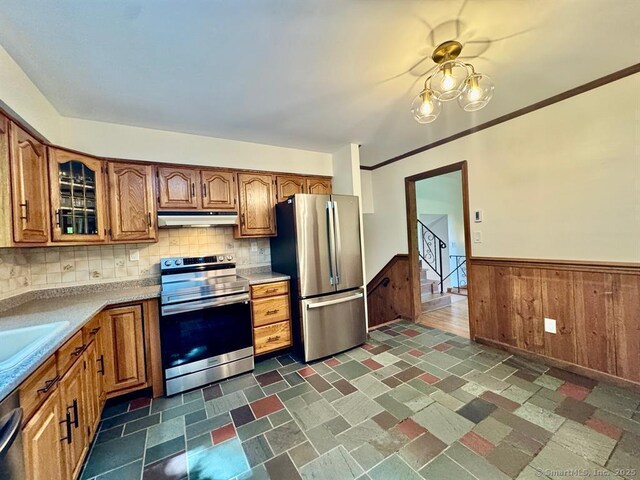 687 Sprout Brook Rd, Putnam Valley, NY 10579 - kitchen with stainless steel appliances, under cabinet range hood, brown cabinetry, wainscoting, and glass insert cabinets