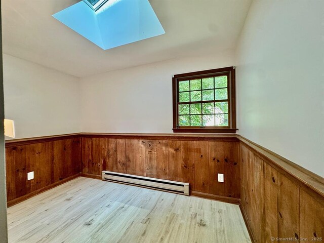 687 Sprout Brook Rd, Putnam Valley, NY 10579 - spare room featuring a baseboard heating unit, a wainscoted wall, a skylight, wooden walls, and wood finished floors