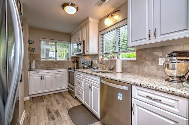 267 Melba St Apt D2, Milford, CT 06460 - kitchen with appliances with stainless steel finishes, white cabinetry, light wood-type flooring, tasteful backsplash, and light stone countertops