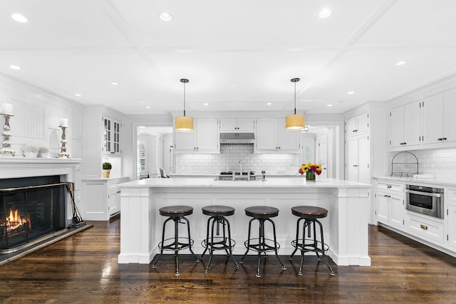 7 Over Rock Ln, Westport, CT 06880 - kitchen with under cabinet range hood, decorative backsplash, white cabinetry, light countertops, and a breakfast bar area