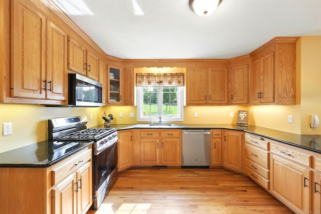 7 Brook Wood Ct, East Windsor, CT 06016 - kitchen featuring appliances with stainless steel finishes, a sink, light wood-type flooring, dark countertops, and glass insert cabinets