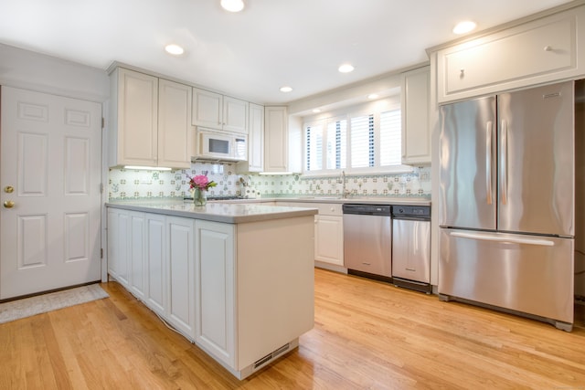 510 W Lyon Farm Dr Unit 510, Greenwich, CT 06831 - kitchen featuring stainless steel appliances, a peninsula, light countertops, light wood-style floors, and decorative backsplash