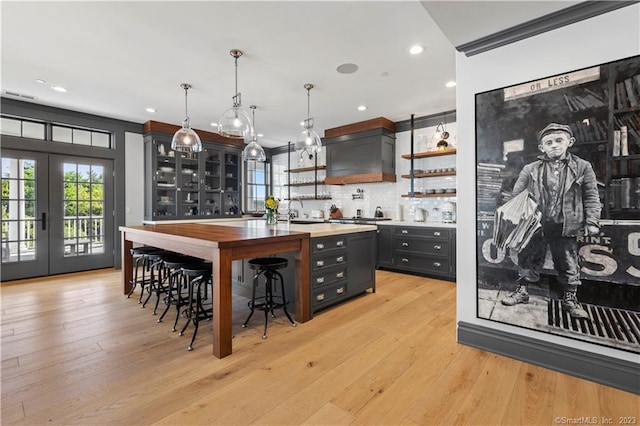 66 High St Unit 17, Guilford, CT 06437 - indoor wet bar with backsplash, french doors, premium range hood, light wood finished floors, and decorative light fixtures
