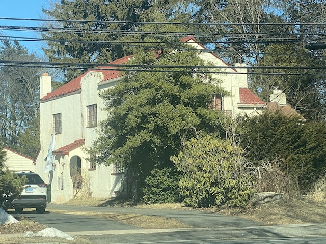 view of side of home featuring a chimney, stucco siding, and a tiled roof