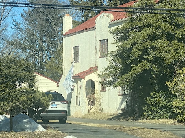 view of front facade with a chimney, stucco siding, and a tile roof
