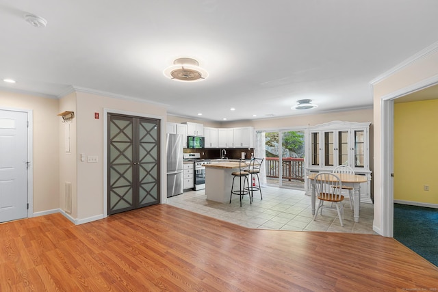 142 Summit St Unit 142, Norwich, CT 06360 - kitchen with appliances with stainless steel finishes, a kitchen bar, light wood-type flooring, white cabinetry, and baseboards