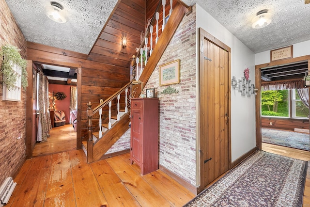 103 Pine St, Columbia, CT 06237 - staircase featuring hardwood / wood-style flooring, brick wall, a textured ceiling, wooden walls, and baseboards