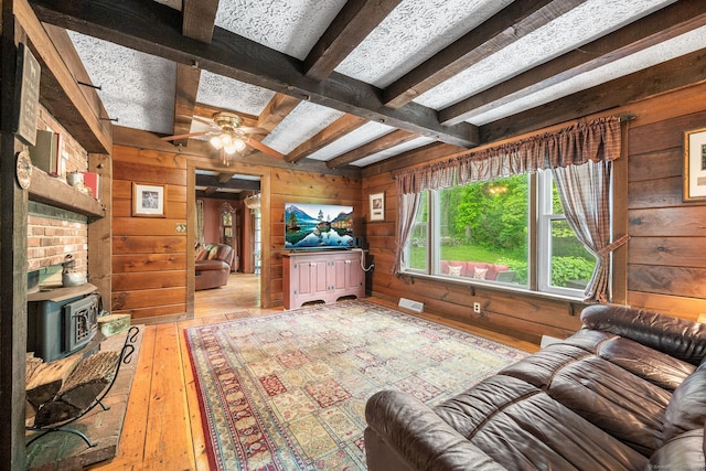103 Pine St, Columbia, CT 06237 - living room with wood walls, beamed ceiling, light wood-type flooring, a ceiling fan, and a wood stove