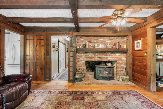 103 Pine St, Columbia, CT 06237 - living area with wood-type flooring, wooden walls, a wood stove, beam ceiling, and ceiling fan