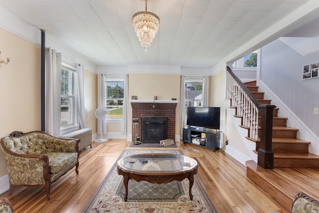 90 Broad St, Killingly, CT 06239 - living room featuring radiator, stairway, a brick fireplace, light wood-type flooring, and a chandelier