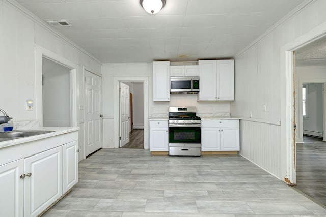 9 Woodland St, Vernon, CT 06066 - kitchen featuring stainless steel appliances, baseboard heating, ornamental molding, white cabinetry, and light countertops