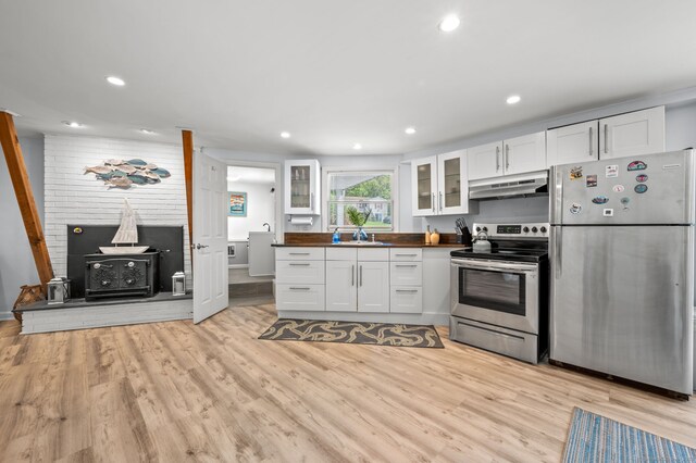 49 Economy Dr, Westbrook, CT 06498 - kitchen with appliances with stainless steel finishes, under cabinet range hood, a wood stove, white cabinets, and a sink