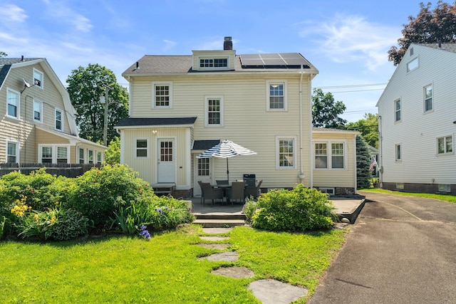 1748 Whitney Ave, Hamden, CT 06517 - rear view of house with roof mounted solar panels, a chimney, a patio area, and roof with shingles