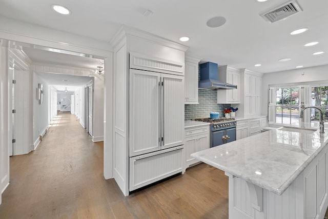15 Mill Rd, New Canaan, CT 06840 - kitchen with wall chimney range hood, a sink, premium appliances, white cabinetry, and wood finished floors