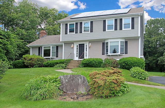 43 Redwood Cir, Shelton, CT 06484 - colonial home featuring roof mounted solar panels, a front yard, a chimney, and a shingled roof