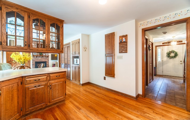 258 New Cheshire Rd, Wallingford, CT 06492 - kitchen with light countertops, light wood-style flooring, a brick fireplace, glass insert cabinets, and brown cabinetry