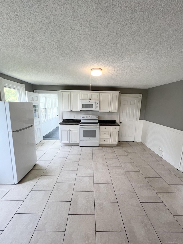 127 Smalley St, New Britain, CT 06051 - kitchen featuring white appliances, dark countertops, wainscoting, a textured ceiling, and light tile patterned floors