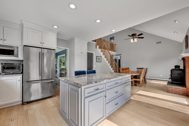 233 Church St, Hebron, CT 06231 - kitchen with stainless steel appliances, a wood stove, a baseboard heating unit, ceiling fan, and white cabinetry
