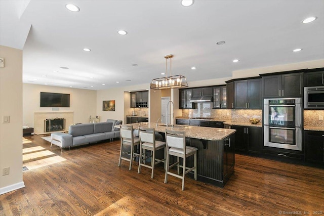 1 Mountaincrest Dr, Cheshire, CT 06410 - kitchen with stainless steel appliances, a kitchen bar, under cabinet range hood, dark wood-style flooring, and light stone counters