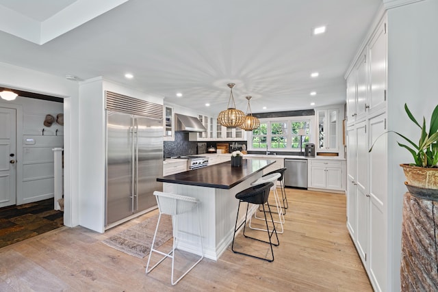 6 Over Rock Ln, Westport, CT 06880 - kitchen with appliances with stainless steel finishes, wall chimney exhaust hood, a kitchen breakfast bar, white cabinets, and decorative backsplash
