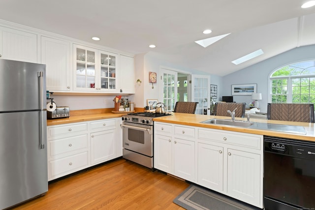 19 Orchard Ln, New Canaan, CT 06840 - kitchen featuring stainless steel appliances, a skylight, light wood-style floors, vaulted ceiling, and glass insert cabinets