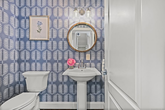 half bath with wallpapered walls, toilet, and baseboards