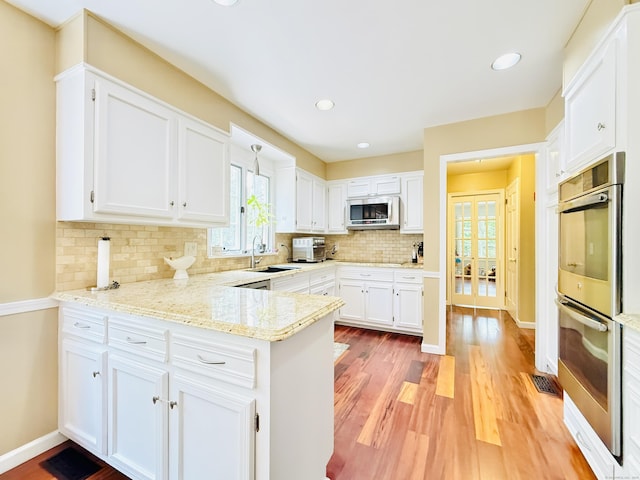 51 Boulder Brook Dr, Stamford, CT 06903 - kitchen with appliances with stainless steel finishes, a peninsula, tasteful backsplash, white cabinetry, and a sink