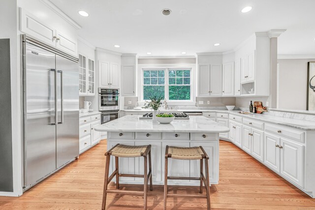 4 Lyons Plain Rd, Weston, CT 06883 - kitchen with stainless steel appliances, ornamental molding, white cabinets, a breakfast bar area, and light wood finished floors