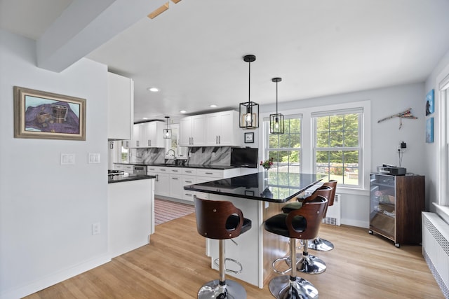 104 Quaker Farm Rd, Groton, CT 06355 - kitchen with radiator, dark countertops, white cabinetry, light wood finished floors, and decorative backsplash