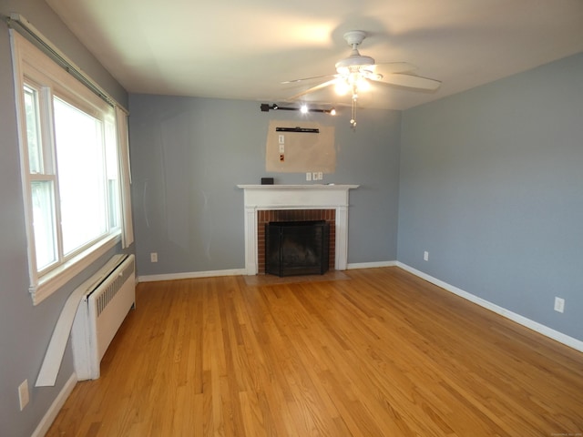 450 Thorme St, Bridgeport, CT 06606 - unfurnished living room with radiator heating unit, light wood-type flooring, a brick fireplace, and healthy amount of natural light