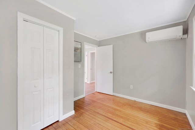 60 Indian Spring Rd, Woodstock, CT 06281 - unfurnished bedroom featuring an AC wall unit, baseboards, crown molding, light wood finished floors, and a closet