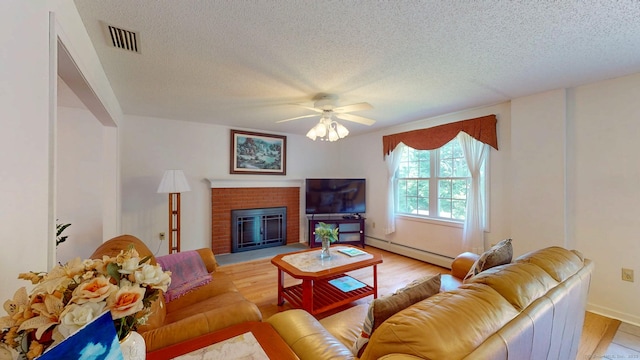 26 Reno Dr, Middletown, CT 06457 - living room featuring baseboard heating, light wood-style flooring, a textured ceiling, a ceiling fan, and a brick fireplace