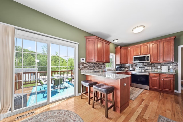 280 Ridgefield Ave, Waterbury, CT 06705 - kitchen featuring appliances with stainless steel finishes, a peninsula, a sink, decorative backsplash, and light wood-style floors