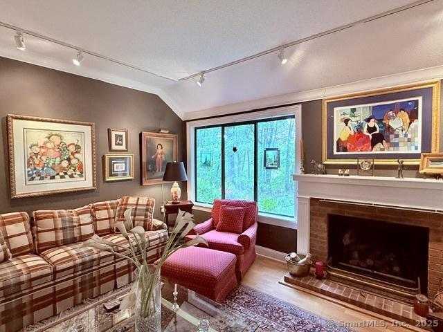 12 Heritage Crst Unit E, Southbury, CT 06488 - living room featuring rail lighting, lofted ceiling, wood finished floors, and a fireplace with raised hearth