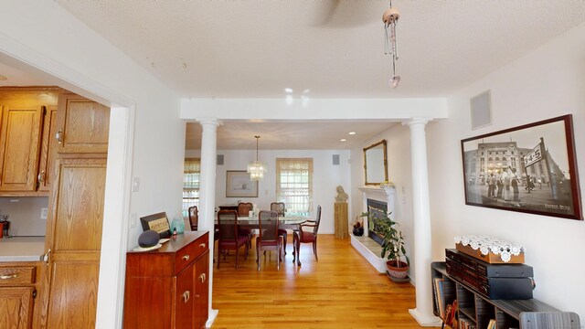 77 Bassett Rd, North Haven, CT 06473 - dining area with ornate columns, light wood-type flooring, a fireplace with raised hearth, and baseboards
