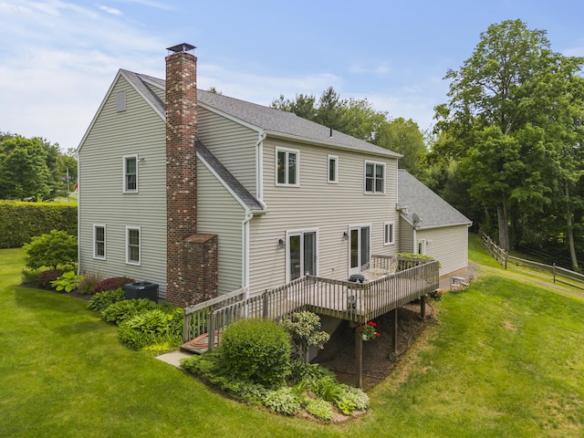 rear view of house featuring a chimney, a wooden deck, a yard, and roof with shingles