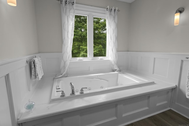 full bathroom featuring a jetted tub, wainscoting, a decorative wall, and wood finished floors