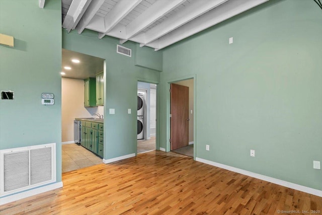 1 Front St Unit 204, New Haven, CT 06513 - spare room featuring stacked washer / dryer, beam ceiling, light wood-style flooring, a high ceiling, and baseboards