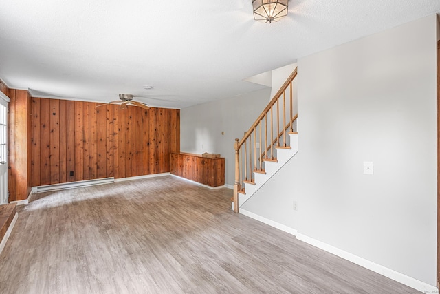 33 Deer Park Rd, Simsbury, CT 06089 - unfurnished living room with baseboard heating, light wood-type flooring, wood walls, stairway, and baseboards